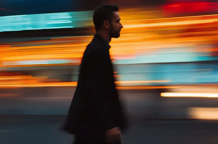 Side profile of a man walking past blurred vibrant lights, conveying urban energy and dynamism.